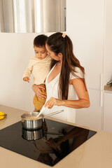 Mom holding baby while cooking rice in kitchen