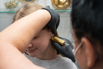 A doctor wearing sterile black medical gloves pierces the ears of a young pretty girl. Girls get...