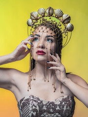 A beautiful, slender woman wearing a crown of seashells covered in gold. She's wearing a tight-fitting dress made of sparkly floats. On a yellow background