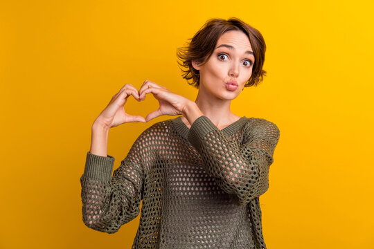 Photo of pretty cute girl dressed stylish clothes demonstrate heart figure sending you sweet air kiss isolated on yellow color background