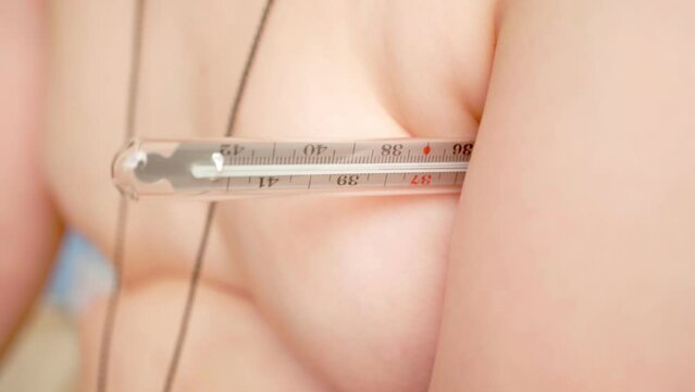 The thermometer is under the arm of a sick child. A close-up of the body temperature measurement process. The thermometer shows 38.4 degrees Celsius.