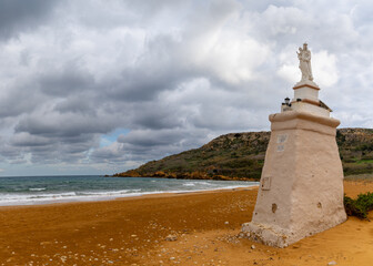 view of the red sand beach and Staue of Our Lady in Ramla Bay on Gozo Island in Malta