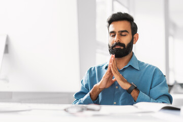 Serene indian businessman meditating for calmness in office