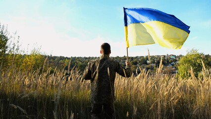 Male soldier of ukrainian army runs with lifted blue-yellow banner at countryside. Young man in...