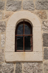 Fototapeta na wymiar Old arched window with metal grill on stone facade in Montenegro