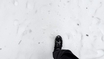 Point of view to male foot stepping on snowy path at winter park. Legs of young man in sneakers...