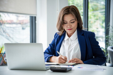 Businesswoman sitting at desk on couch in workplace or at home working on laptop and analyzing data...