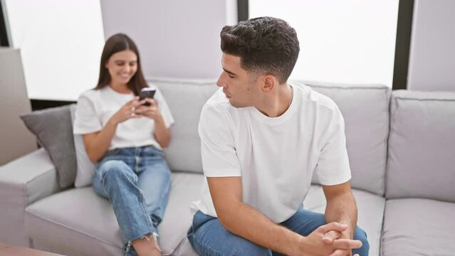A man and woman engaged with their smartphones separately on a cozy sofa in a well-lit modern living room