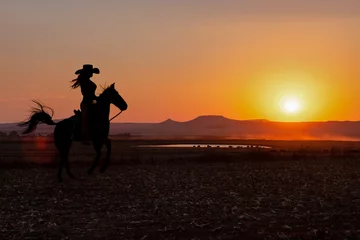Foto op Plexiglas silhouette cowgirl in the sunset riding in the prairie near a waterhole © poco_bw
