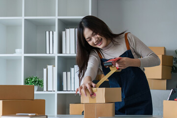 Young asian woman taping up a cardboard box in home office SME e-commerce business, relocation and...
