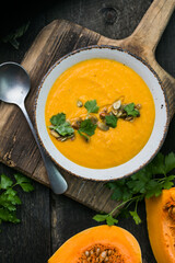 Pumpkin soup and organic pumpkins on wooden table. Seasonal autumn food - Spicy pumpkin soup in bowl.