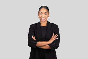 Confident African American businesswoman in a sleek black suit stands with arms crossed