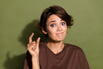Portrait of confused funny girl with short hair wear oversize t-shirt fingers showing small size object isolated on green color background