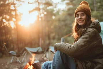Foto op Aluminium Beautiful young woman with brunette hair camping in the forest wilderness, sitting in a camping chair, smiling and looking at the camera. Enjoying morning sunshine in the woods, happy female camper © Nemanja