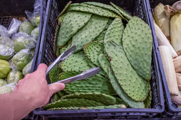 a male hand holds a pair of tongs and takes cactus leaves in a supermarket. healthy lifestyle....