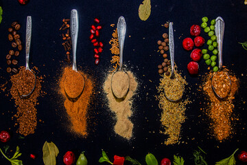 Scattered spices on teaspoons on a black background next to other colorful products