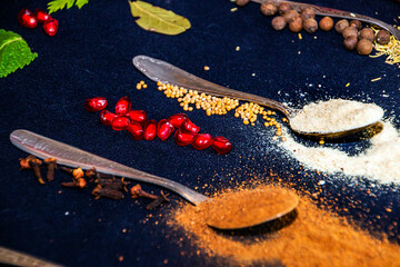 Scattered spices on two teaspoons on a black background next to other colorful products close-up