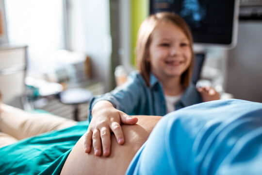 Little girl holding pregnant mothers belly during examination