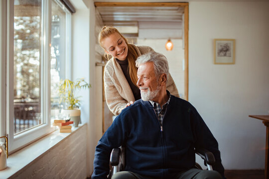 Smiling young woman with elderly man in wheelchair by the window