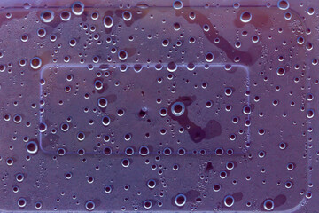 Close-up of water droplets on a smooth purple plastic surface creating a textured pattern.