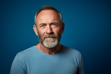 Portrait of a senior man with grey hair and beard on blue background