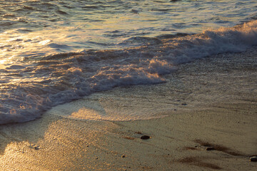 Golden sunset light reflecting on the sea waves at a sandy beach