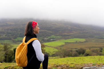Latin woman on her visit to rural Ireland standing next to a stone wall to see a splendid landscape...