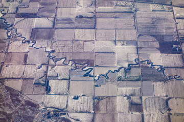 A river meanders its way through several agricultural fields in the rural farmland area of Colorado. Picture taken from high above in a plane during the winter.