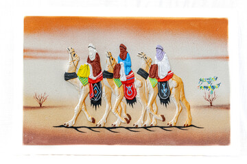 Sand painting of three tuareg people wearing colorful clothings riding dromedary camels walking on...