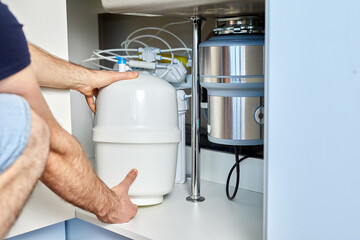 A plumber installs reverse osmosis equipment under the sink. The master installs a water filter in...