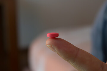 Close-up of a finger holding a pink pill with blurred background