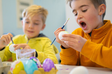 Excited children painting easter eggs with brush and paint