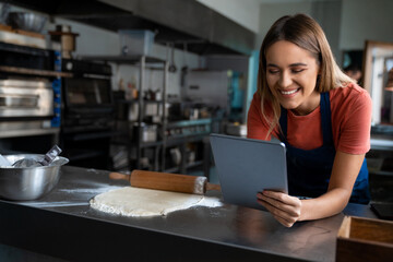 Smiling young woman baker using digital tablet at work in the pastry kitchen.