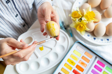 Obraz na płótnie Canvas A brush in the process of painting Easter eggs with watercolors. The concept of preparing for Easter. View from above.