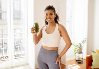 Cheerful fitness woman holding bottle of homemade detox drink indoors