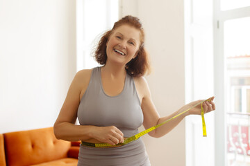 Happy senior woman measuring her waist with tape, showing her fitness progress