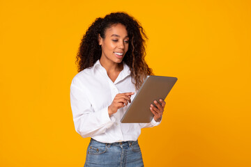 Happy young black woman using tablet computer over yellow background