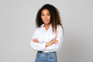 Black young lady crosses hands standing with confidence, gray backdrop