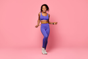 Young athletic black woman measuring waist showcasing fitness progress, studio