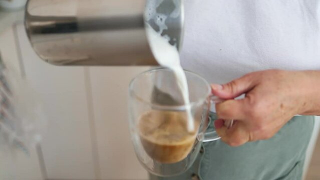 Closeup of female hands pouring milk and preparing fresh cappuccino, coffee artist and preparation concept, morning coffee. High quality FullHD footage