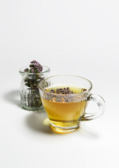 oregano tea in a glass cup and a jar with dry oregano herb on a white table