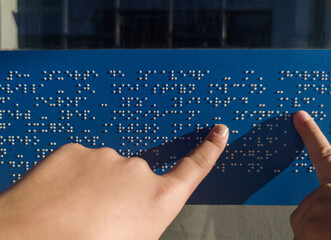Child hands reading text caption in braille language at bus stop glass