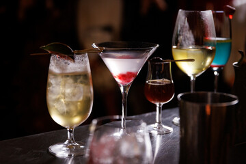 Collection of colorful cocktails on a bar counter with a blurred background of people enjoying their drinks.