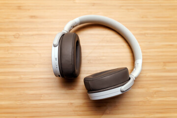 The pair of wireless headphones on a wooden surface. The headphones are white with brown ear cushions and have a modern design.