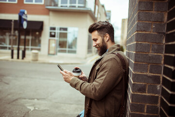 Obraz na płótnie Canvas Man walking with coffee and using smartphone in city street