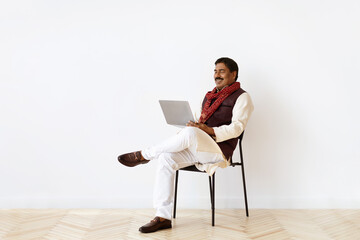 Mature indian man using laptop, white wall background