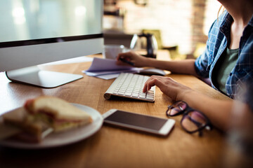Freelancer working on computer with breakfast sandwich on desk