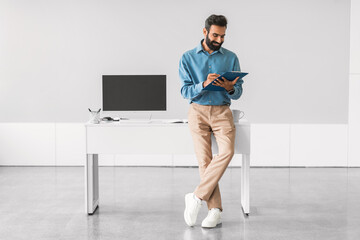 Engaged indian businessman reading tablet by his workstation