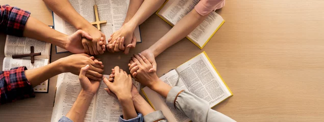 Fotobehang Cropped image of group of people praying together while holding hand on holy bible book at wooden church. Concept of hope, religion, faith, christianity and god blessing. Top view. Burgeoning. © Summit Art Creations