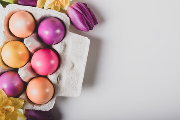 Colorful naturally dyed Easter eggs in egg box on white background, top view, flat lay style. Copy space for text.
